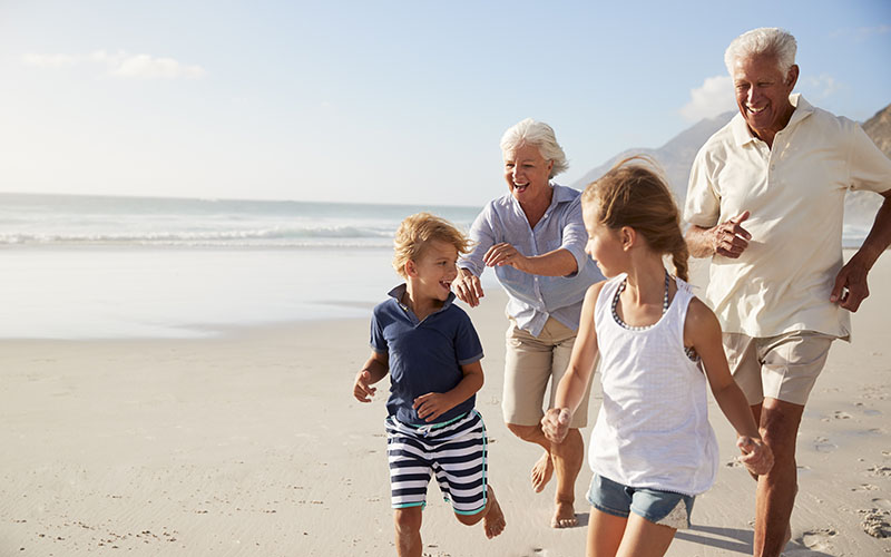 Grandparents Running Along Beach With Grandchildren On Summer Vacation